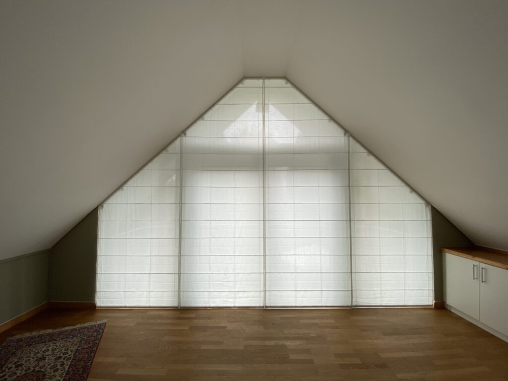 Maßgefertigte Biesenfaltrollos für schräge Fenster in einem lichtdurchfluteten Dachgeschoss.