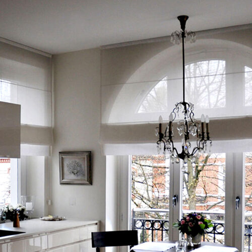 Lichtdurchlässige Biesenfaltrollos aus Leinenstoff vor Rundbogenfenstern in einer modernen Küche.