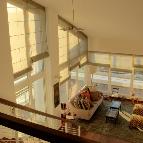 Maßgefertigte Biesenfaltrollos mit Volantabschluss für hohe Fenster und Schräge, in warmem Leinenstoff, harmonisch auf die Architektur abgestimmt.