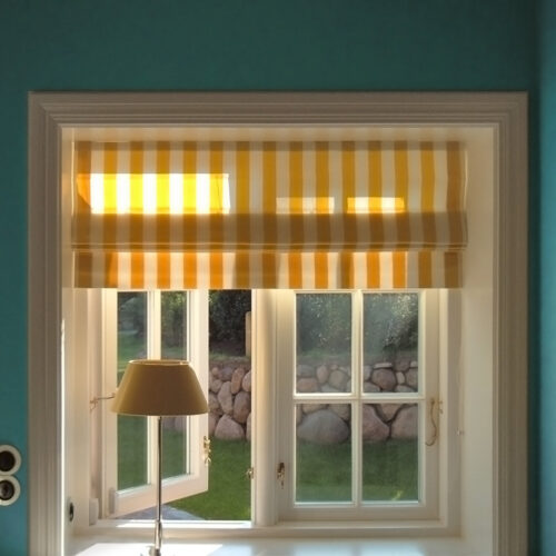 Faltrollo mit gelben Blockstreifen, geradem Rolloabschluss (Volant) und Schnurzuganlage vor einem klassischen Sprossenfenster.