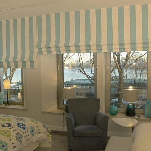 Faltrollos mit hellblauen Blockstreifen als stilvolle Fensterdekoration im Schlafzimmer.