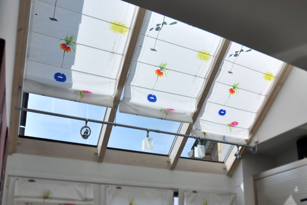 Maßgefertigte Faltrollos für Dachflächenfenster mit leichtem Stoff und floralem Design.