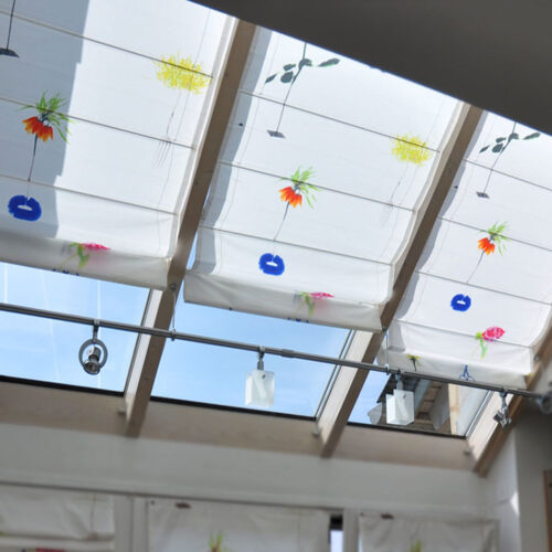 Maßgefertigte Faltrollos für Dachflächenfenster mit leichtem Stoff und floralem Design.