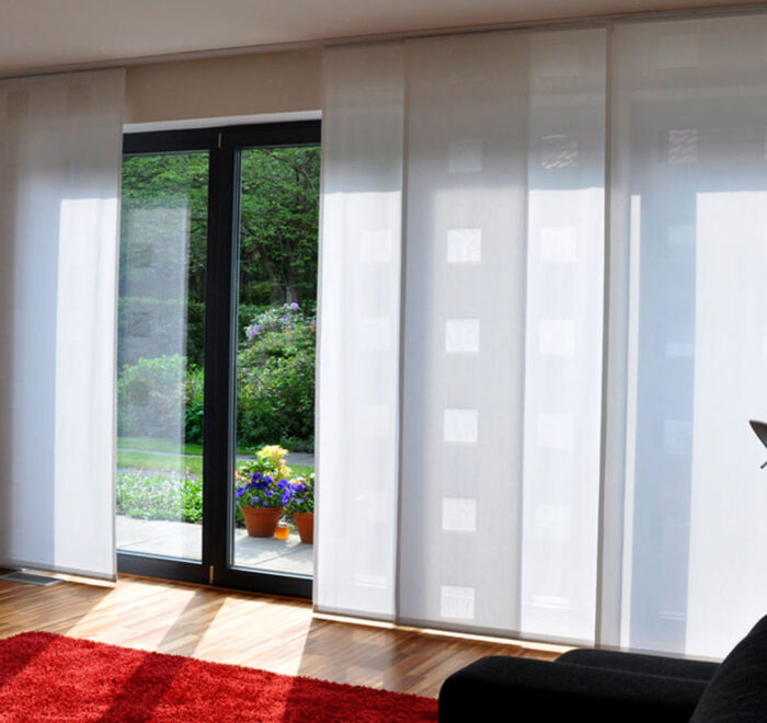 Moderne Flächenvorhänge aus weißem Ausbrenner-Stoff vor einer großen Fensterfront.