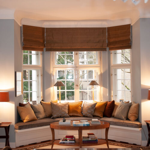 Gemütliche Fensternische mit maßgefertigten Raffrollos in warmen Brauntönen.