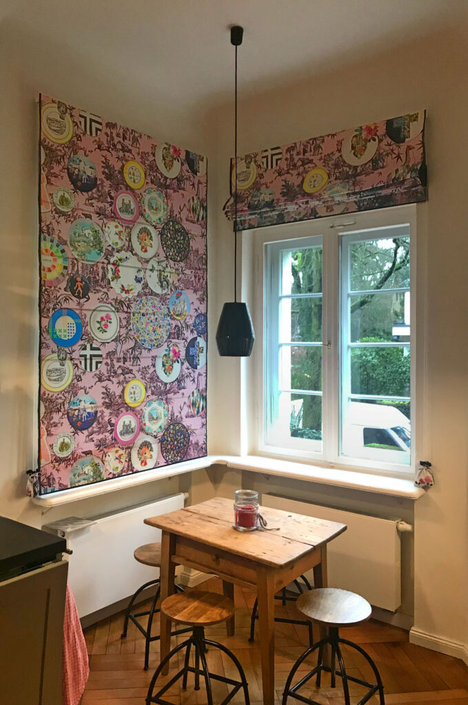 Gefütterte Quadro Faltrollos mit buntem Druckmotiv und eleganter schwarzer Einfassung.