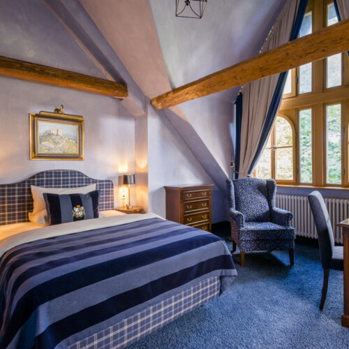 Elegantes Schlosshotel-Zimmer mit gemütlichem Ambiente, rustikalen Holzbalken und maßgefertigten, abgeschrägten Vorhängen.