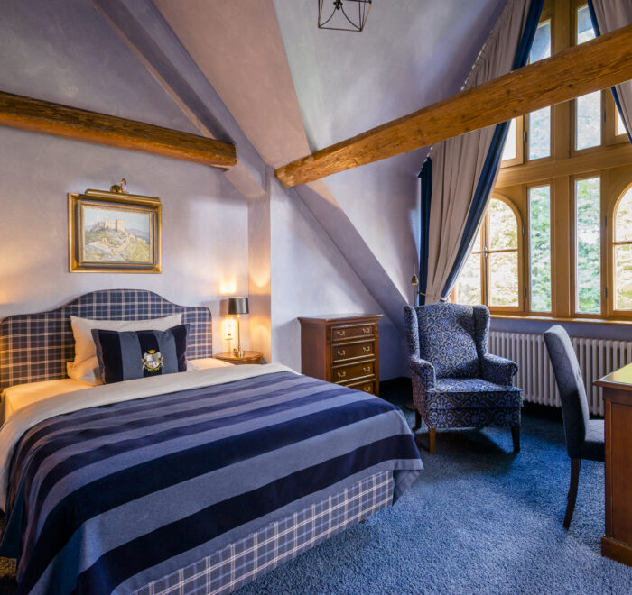 Elegantes Schlosshotel-Zimmer mit gemütlichem Ambiente, rustikalen Holzbalken und maßgefertigten, abgeschrägten Vorhängen.