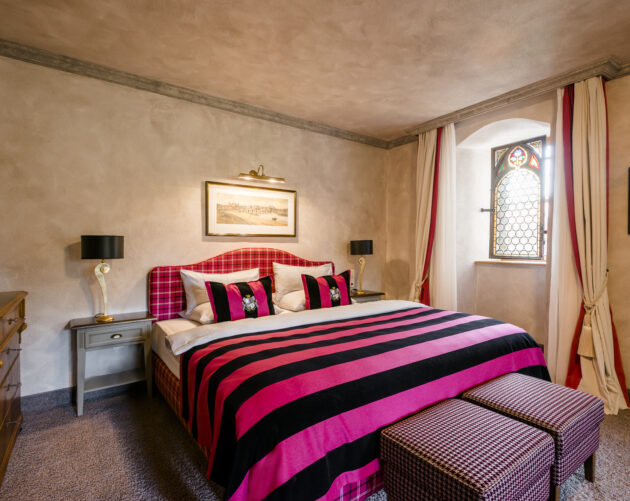 Elegantes Zimmer in einem Schlosshotel mit kunstvoll drapierten Vorhängen in Cremeweiß und Rot vor einem historischen Bogenfenster.