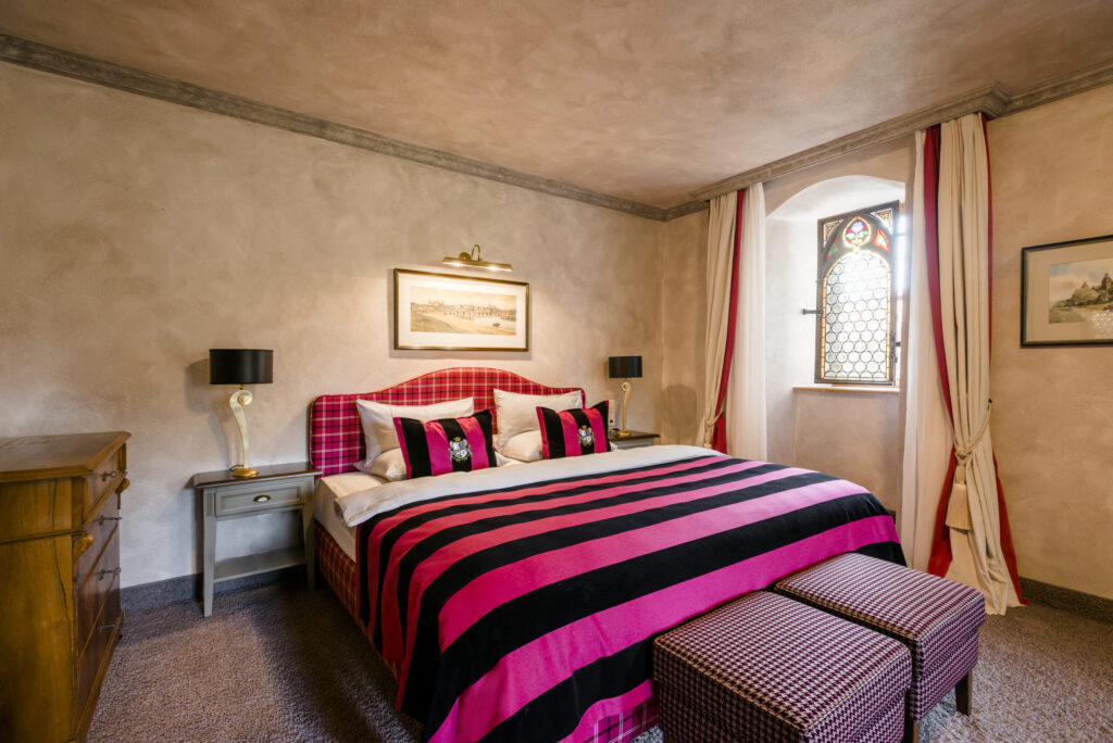 Elegantes Zimmer in einem Schlosshotel mit kunstvoll drapierten Vorhängen in Cremeweiß und Rot vor einem historischen Bogenfenster.