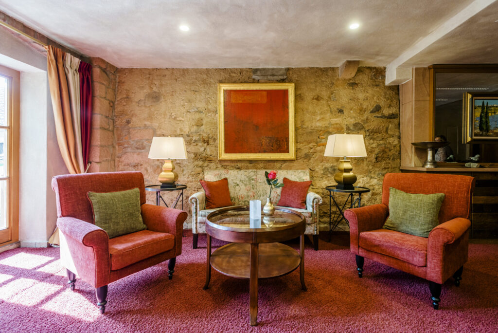 Einladende Hotellobby mit roten Polstersesseln, stilvollen Kissen und bodenlangen Vorhängen.