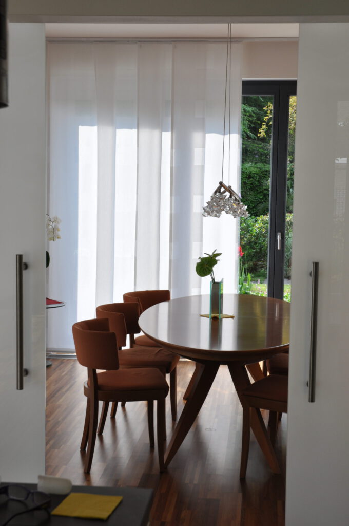 Elegante Flächenvorhänge aus Ausbrenner-Stoff in einem stilvollen Esszimmer mit großem Holztisch.