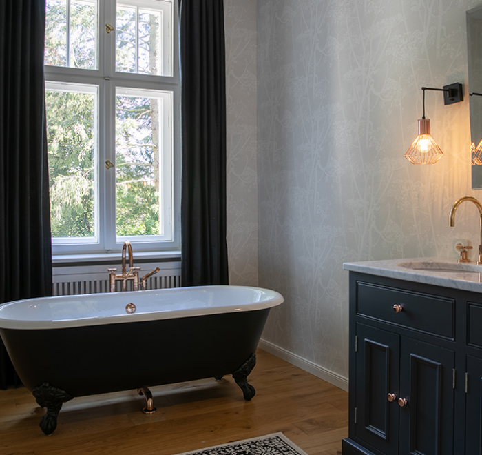 Elegantes Badezimmer mit freistehender, schwarzer Badewanne und dunklen Vorhängen.