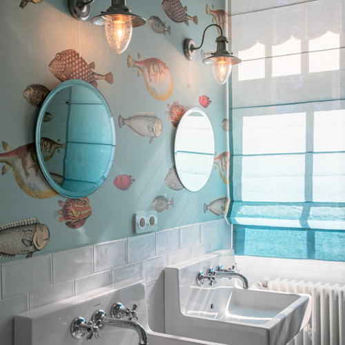Helles Badezimmer mit maritimer Tapete und türkisfarbenem Biesenfaltrollo, das das Sonnenlicht sanft filtert.