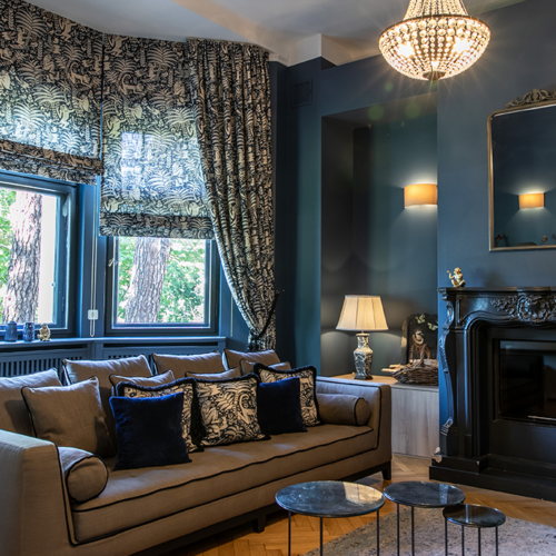 Eleganter Wohnraum mit Raffrollos, Vorhängen und Kissen im klassischen Muster, kombiniert mit dunklen Wänden und luxuriösen Details.