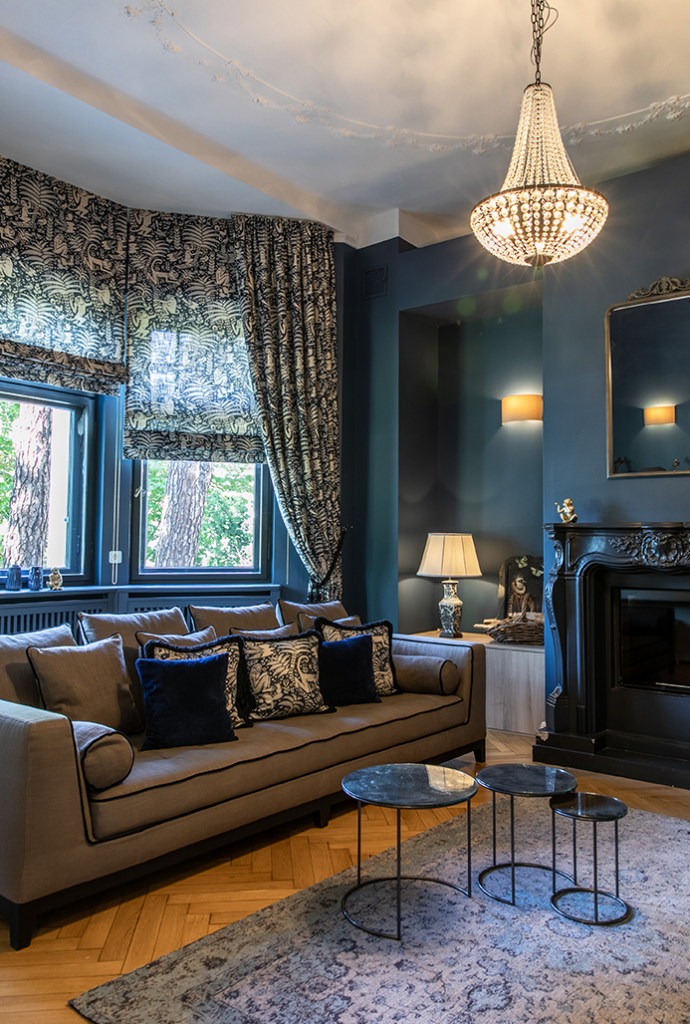 Eleganter Wohnraum mit Raffrollos, Vorhängen und Kissen im klassischen Muster, kombiniert mit dunklen Wänden und luxuriösen Details.