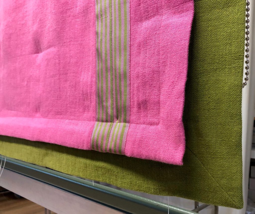 Heruntergelassenes Raffrollo in Pink mit grüner Unterlegung und Besatzstreifen in kontrastierendem Design.