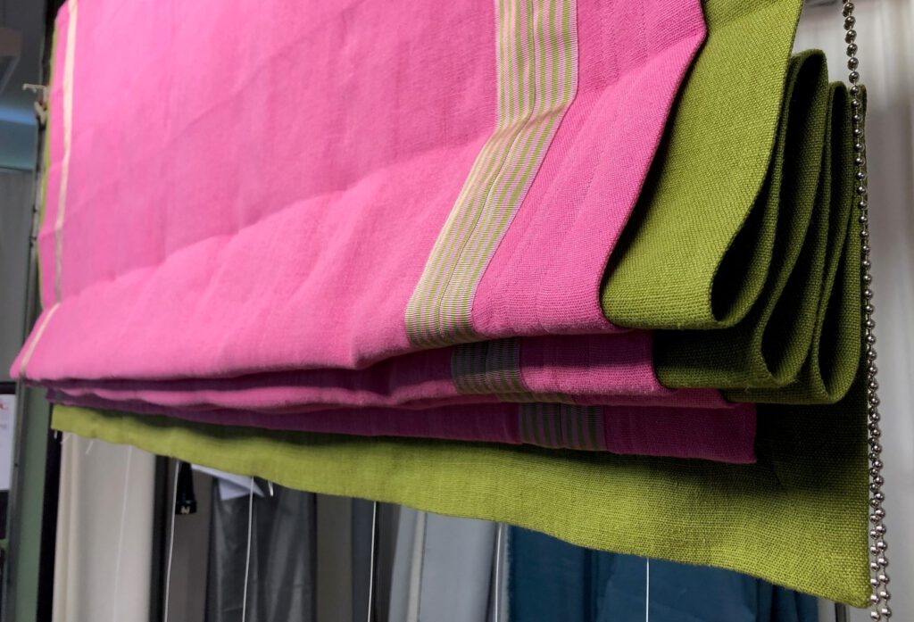 Hochgezogenes Raffrollo in Pink mit grüner Unterlegung und Besatzstreifen in kontrastierendem Design.