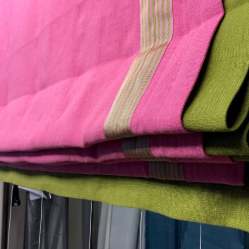 Hochgezogenes Raffrollo in Pink mit grüner Unterlegung und Besatzstreifen in kontrastierendem Design.