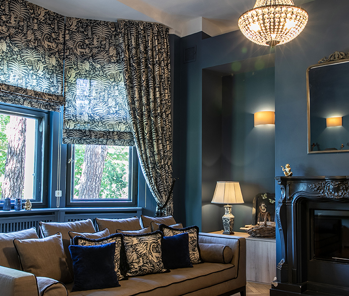 Eleganter Wohnraum mit Raffrollos, Vorhängen und Kissen im klassischen Muster, kombiniert mit dunklen Wänden und luxuriösen Details.